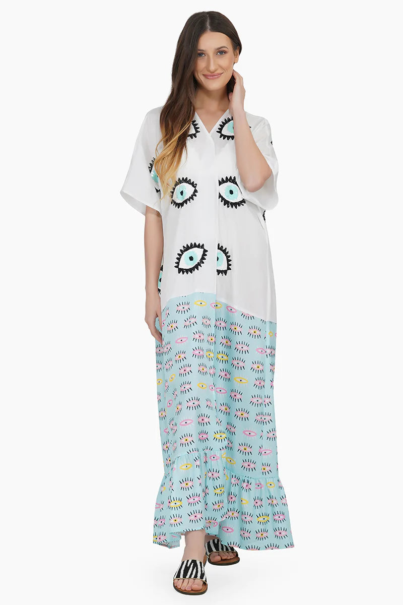 Image features front of the Eye-O-Eye Kaftan features multiple sequined eye all over the top of the design. On the bottom of the maxi length features a blue pattern with yellow and pink eyes throughout. The bottom is ruffled and the kaftan features short sleeves and a silk appearance and feel.